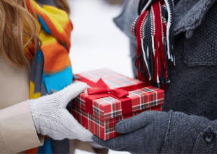 Das perfekte Last Minute Weihnachtsgeschenk, Pärchen überreicht sich im Schnee ein Päckchen