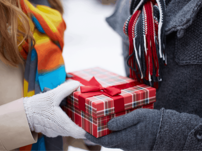 Das perfekte Last Minute Weihnachtsgeschenk, Pärchen überreicht sich im Schnee ein Päckchen